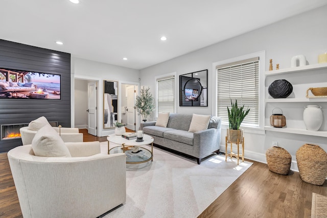 living area with a large fireplace, baseboards, wood finished floors, built in shelves, and recessed lighting