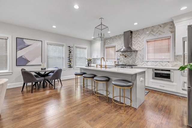 kitchen featuring dark wood-style floors, light countertops, wall chimney range hood, oven, and a kitchen bar