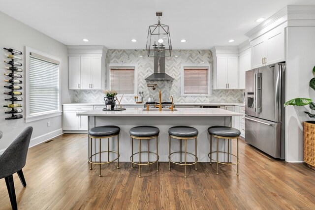 kitchen featuring wall chimney exhaust hood, light countertops, wood finished floors, and stainless steel fridge with ice dispenser