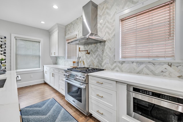 kitchen featuring white cabinets, light wood-style flooring, appliances with stainless steel finishes, light countertops, and wall chimney range hood