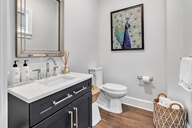 half bathroom featuring baseboards, vanity, toilet, and wood finished floors