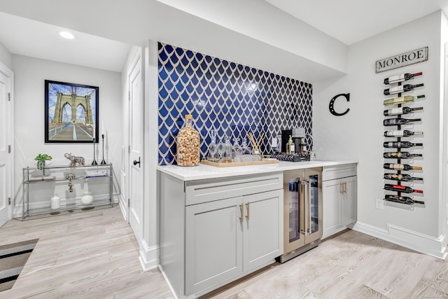 wine cellar with beverage cooler, baseboards, light wood-style flooring, a sink, and recessed lighting