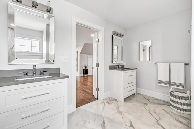 full bath featuring marble finish floor, baseboards, two vanities, and a sink