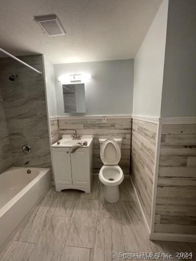 full bathroom with tile patterned flooring, tile walls, toilet, vanity, and tiled shower / bath combo