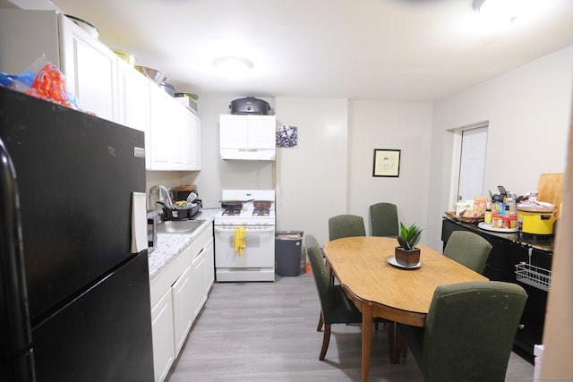 kitchen with black refrigerator, white cabinetry, white range with gas cooktop, and light wood-type flooring