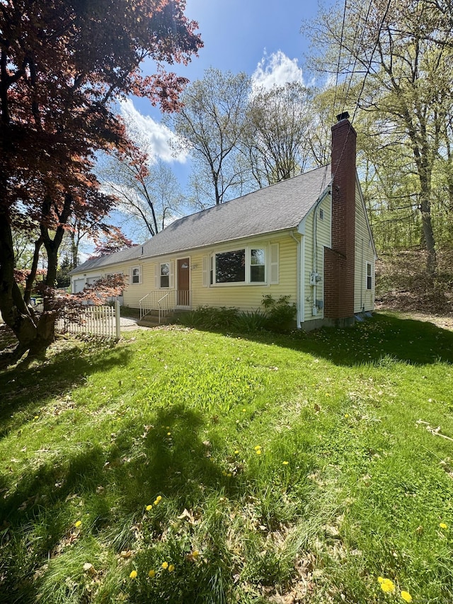 view of front of house featuring roof with shingles, fence, a front yard, and a chimney