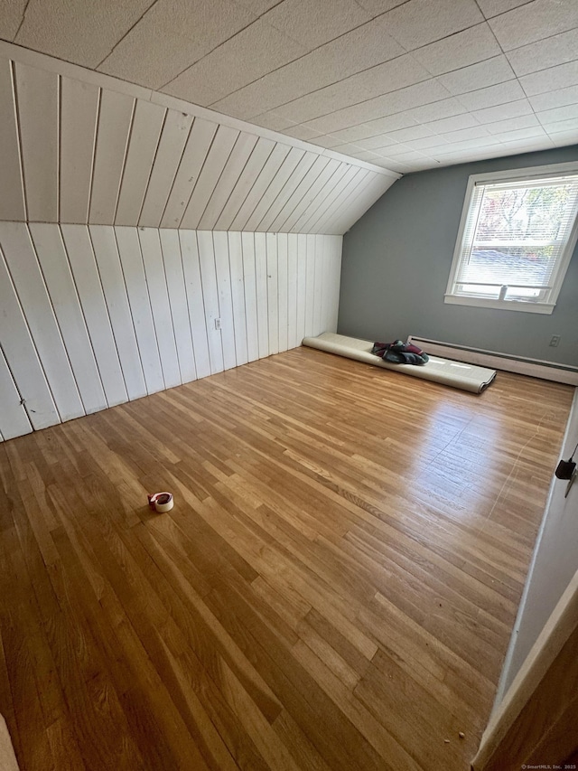 additional living space with wooden walls, a baseboard radiator, vaulted ceiling, and wood finished floors