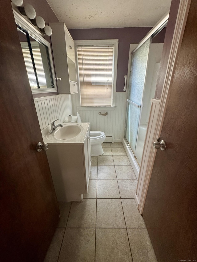 bathroom with tile patterned flooring, vanity, toilet, a wainscoted wall, and a stall shower