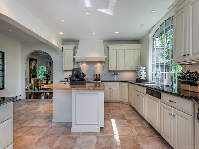 kitchen with sink, dark stone counters, a center island, custom range hood, and cream cabinetry