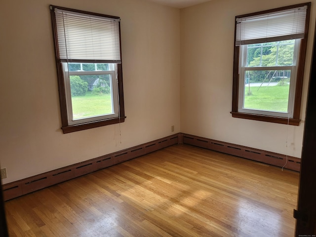 unfurnished room featuring light hardwood / wood-style floors, a baseboard heating unit, and a healthy amount of sunlight