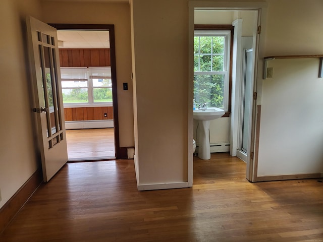 corridor with baseboard heating, plenty of natural light, and light wood-type flooring