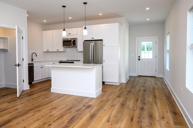 kitchen featuring appliances with stainless steel finishes, white cabinets, hanging light fixtures, and hardwood / wood-style floors