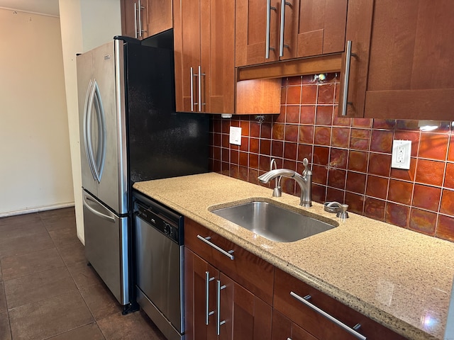 kitchen with dark tile patterned floors, light stone counters, stainless steel dishwasher, decorative backsplash, and sink