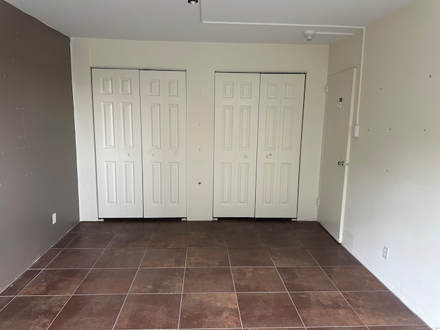 unfurnished bedroom featuring multiple closets and dark tile patterned flooring