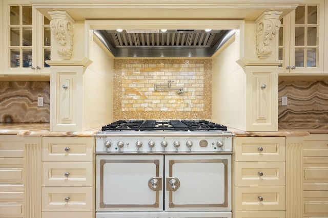 kitchen featuring high end range, cream cabinetry, and backsplash