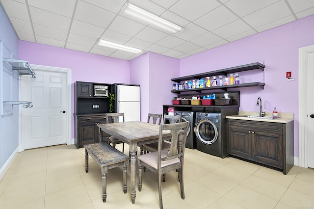 dining space with sink, a drop ceiling, independent washer and dryer, and light tile patterned floors