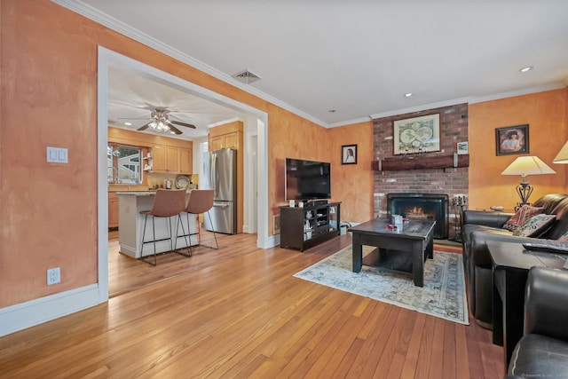 living room with ceiling fan, ornamental molding, a fireplace, and light hardwood / wood-style flooring