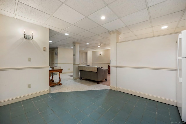 basement featuring a paneled ceiling, tile patterned flooring, and white refrigerator