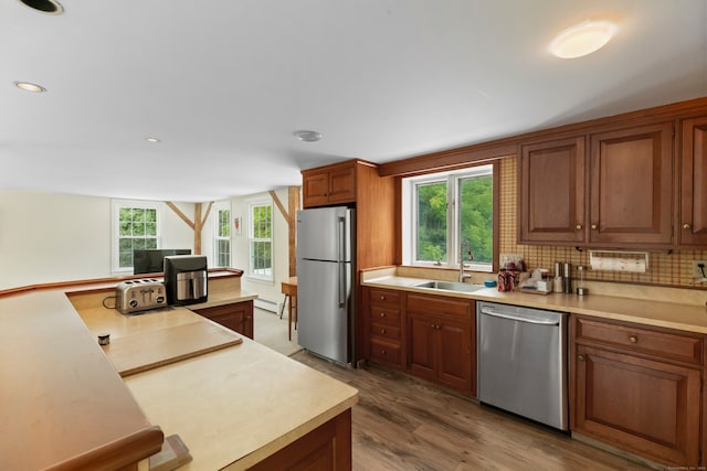 kitchen with backsplash, hardwood / wood-style floors, a baseboard heating unit, stainless steel appliances, and sink