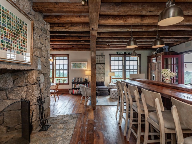 dining room featuring a bar, wood-type flooring, beamed ceiling, and baseboards