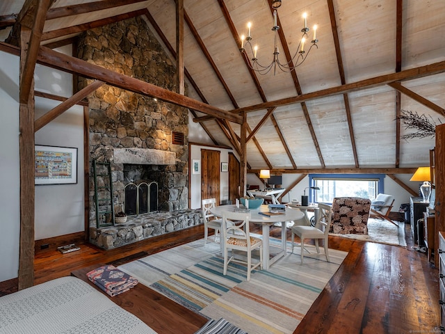 living area featuring wood-type flooring, a notable chandelier, a stone fireplace, and vaulted ceiling with beams