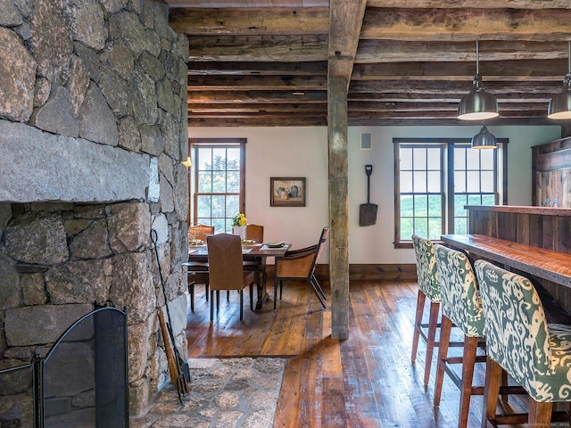 dining area with a healthy amount of sunlight, beam ceiling, hardwood / wood-style floors, and a stone fireplace