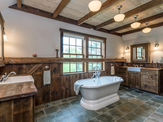 bathroom with a freestanding bath, beam ceiling, wainscoting, and stone tile flooring