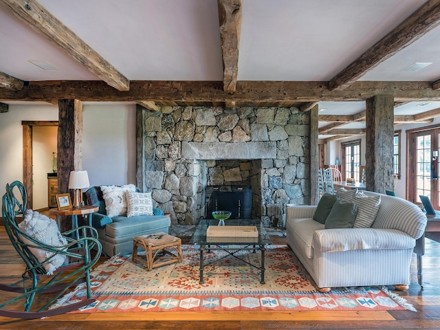 living room featuring beam ceiling, hardwood / wood-style floors, a stone fireplace, and french doors