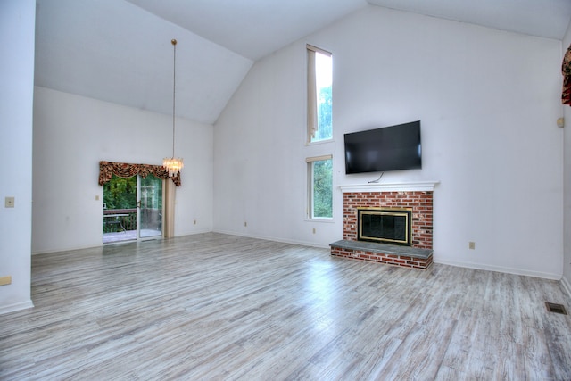 unfurnished living room with high vaulted ceiling, a brick fireplace, a chandelier, and light wood-type flooring