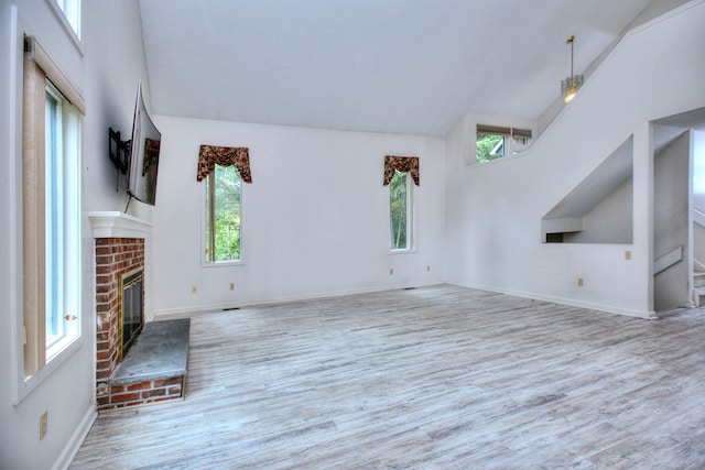 unfurnished living room featuring a fireplace, light hardwood / wood-style floors, high vaulted ceiling, and a wealth of natural light