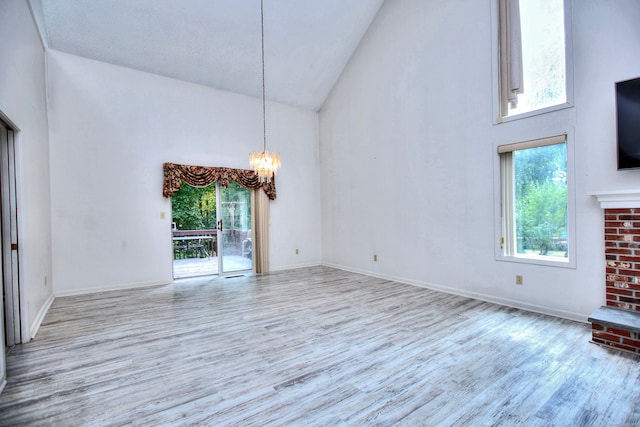 unfurnished living room with light wood-type flooring, a healthy amount of sunlight, a notable chandelier, and high vaulted ceiling