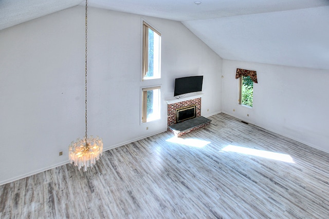 unfurnished living room featuring a notable chandelier, a brick fireplace, lofted ceiling, and light hardwood / wood-style floors