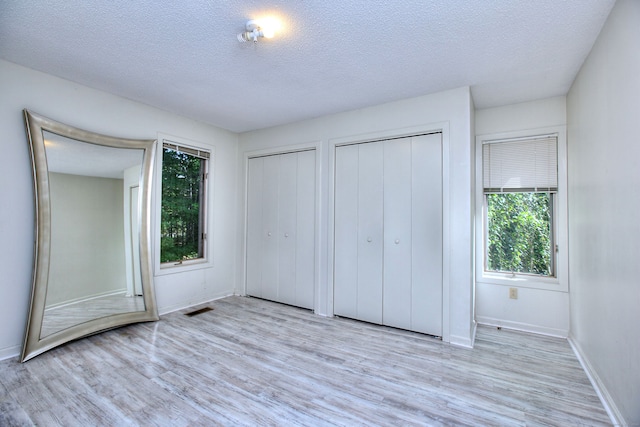 unfurnished bedroom featuring a textured ceiling, light hardwood / wood-style floors, and two closets