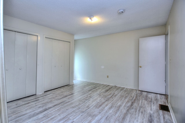 unfurnished bedroom with a textured ceiling, light hardwood / wood-style flooring, and two closets