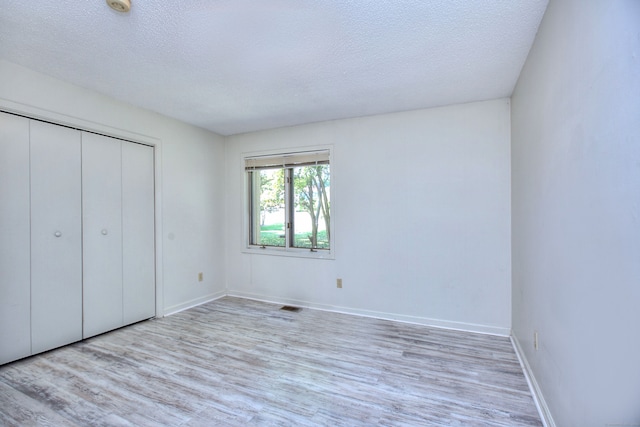 unfurnished bedroom with light wood-type flooring, a textured ceiling, and a closet