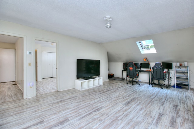 home office with a textured ceiling, lofted ceiling with skylight, and light hardwood / wood-style flooring