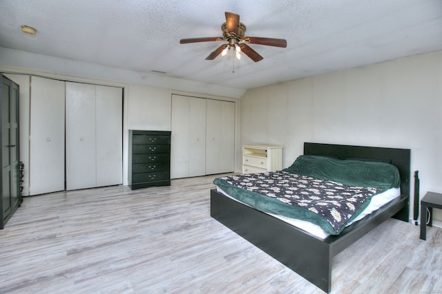 bedroom with a textured ceiling, light hardwood / wood-style floors, two closets, and ceiling fan