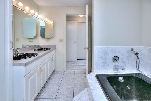 bathroom with tile patterned floors, a textured ceiling, tiled bath, and vanity