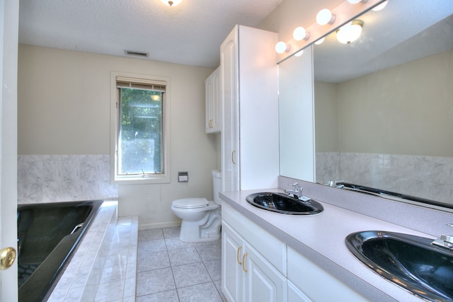 bathroom with vanity, toilet, a relaxing tiled tub, a textured ceiling, and tile patterned flooring