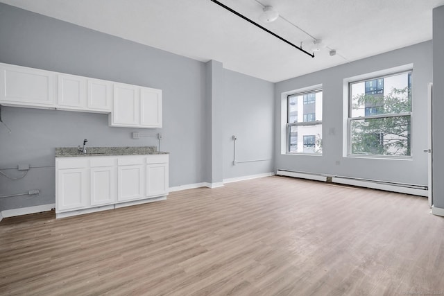 unfurnished living room with light wood finished floors, baseboards, baseboard heating, and a sink