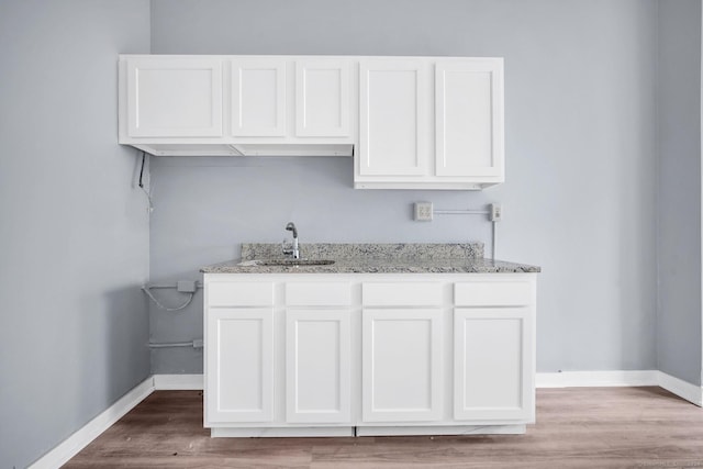 kitchen featuring light stone countertops, baseboards, white cabinets, and a sink