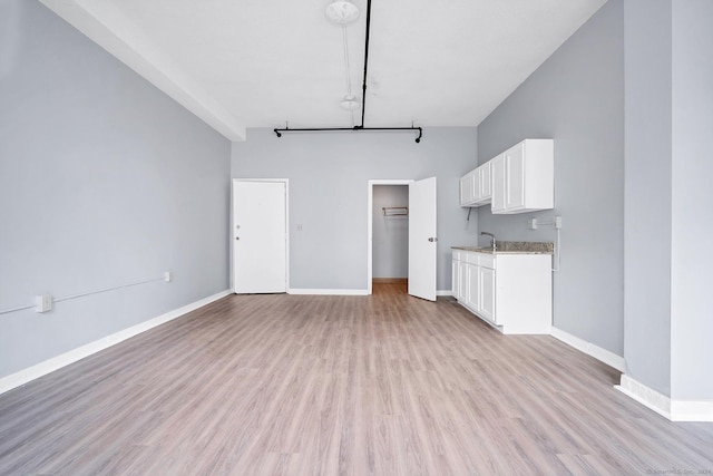 unfurnished living room with light wood-style flooring, a high ceiling, and baseboards