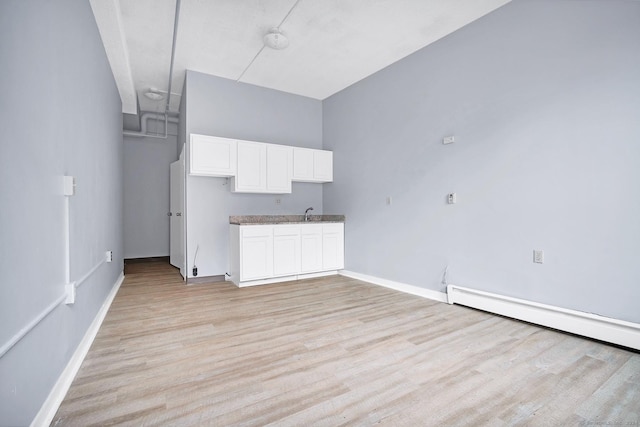 kitchen with light wood-type flooring, a baseboard radiator, baseboards, and white cabinets