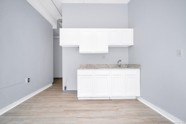 kitchen with white cabinetry, a sink, light wood-style flooring, and light stone countertops