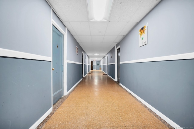 corridor with a drop ceiling, baseboards, and tile patterned floors