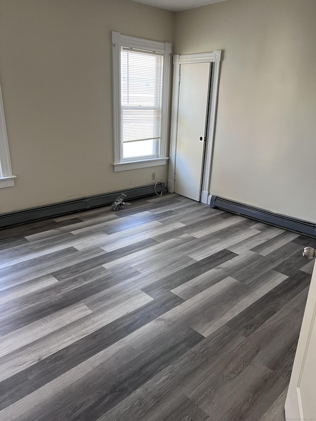 spare room featuring a baseboard heating unit and dark wood-style flooring