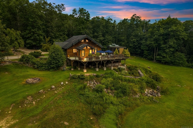 back house at dusk with a wooden deck and a lawn