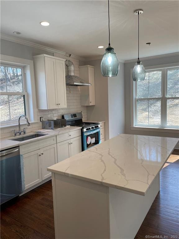 kitchen featuring wall chimney exhaust hood, a center island, hanging light fixtures, stainless steel appliances, and white cabinets