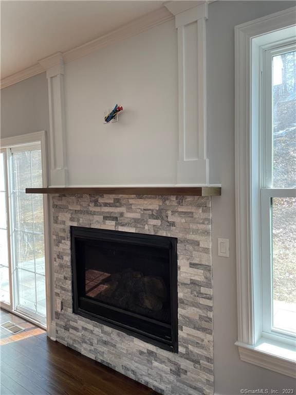 interior details featuring a stone fireplace, wood-type flooring, and ornamental molding