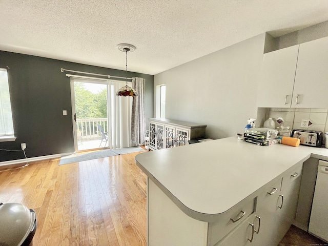 kitchen featuring hanging light fixtures, tasteful backsplash, light hardwood / wood-style floors, a textured ceiling, and kitchen peninsula